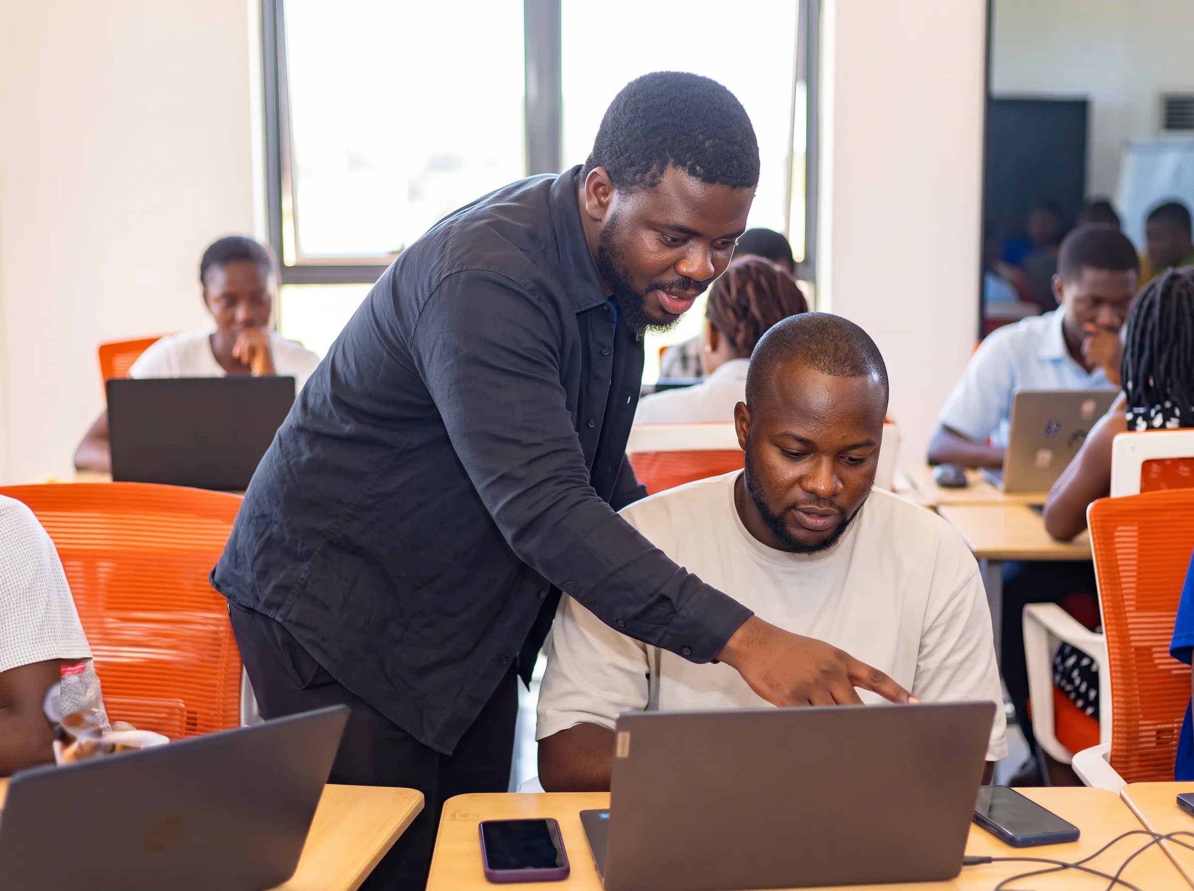 Un mentor accompagne un participant devant son ordinateur, en salle de formation.